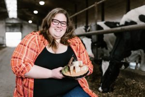 Maryse Vallières-Murray dans une étable et présentant un plateau de fromages